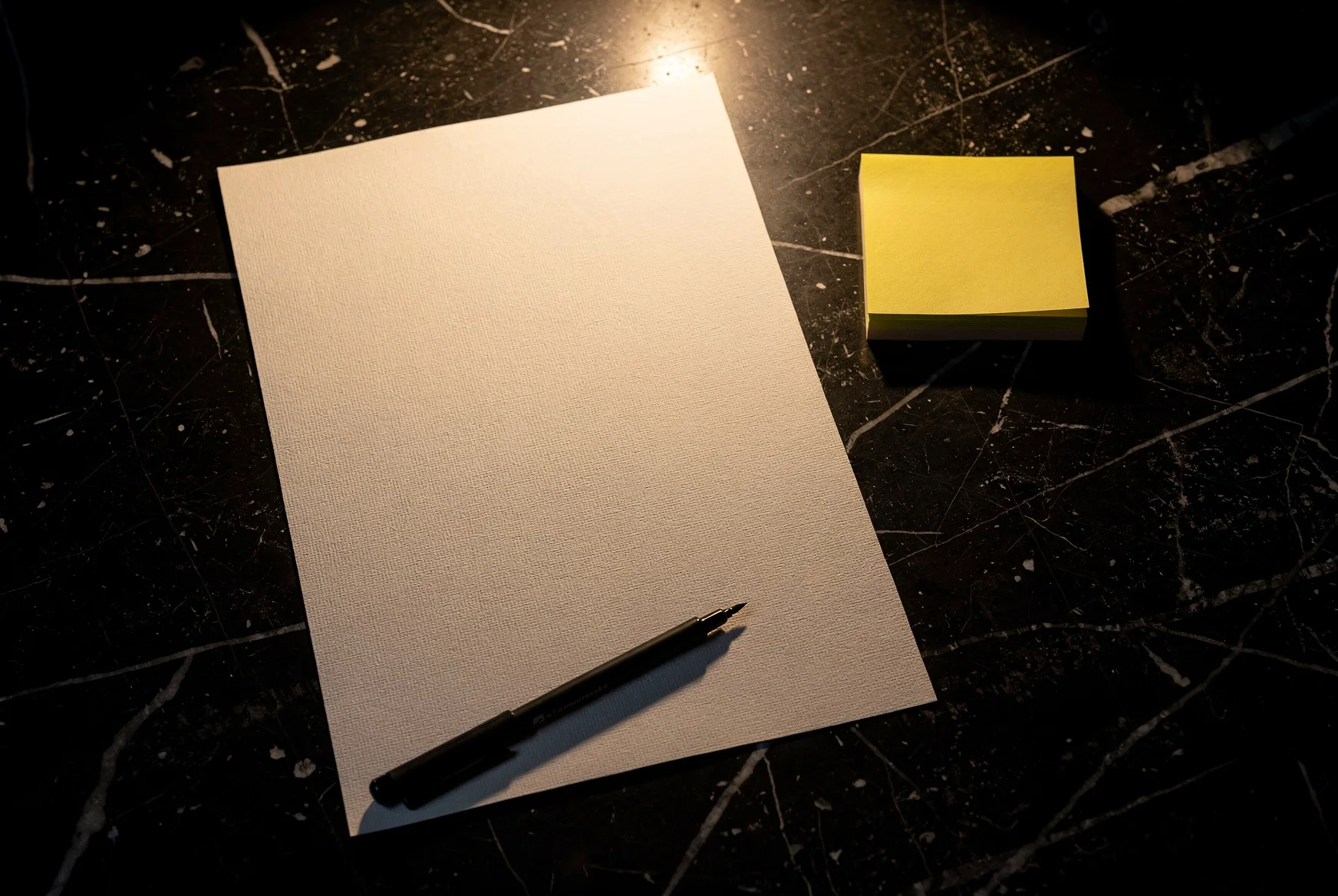 A blank sheet of sketch paper, a black marker and a pad of canary sticky notes on the marble table.